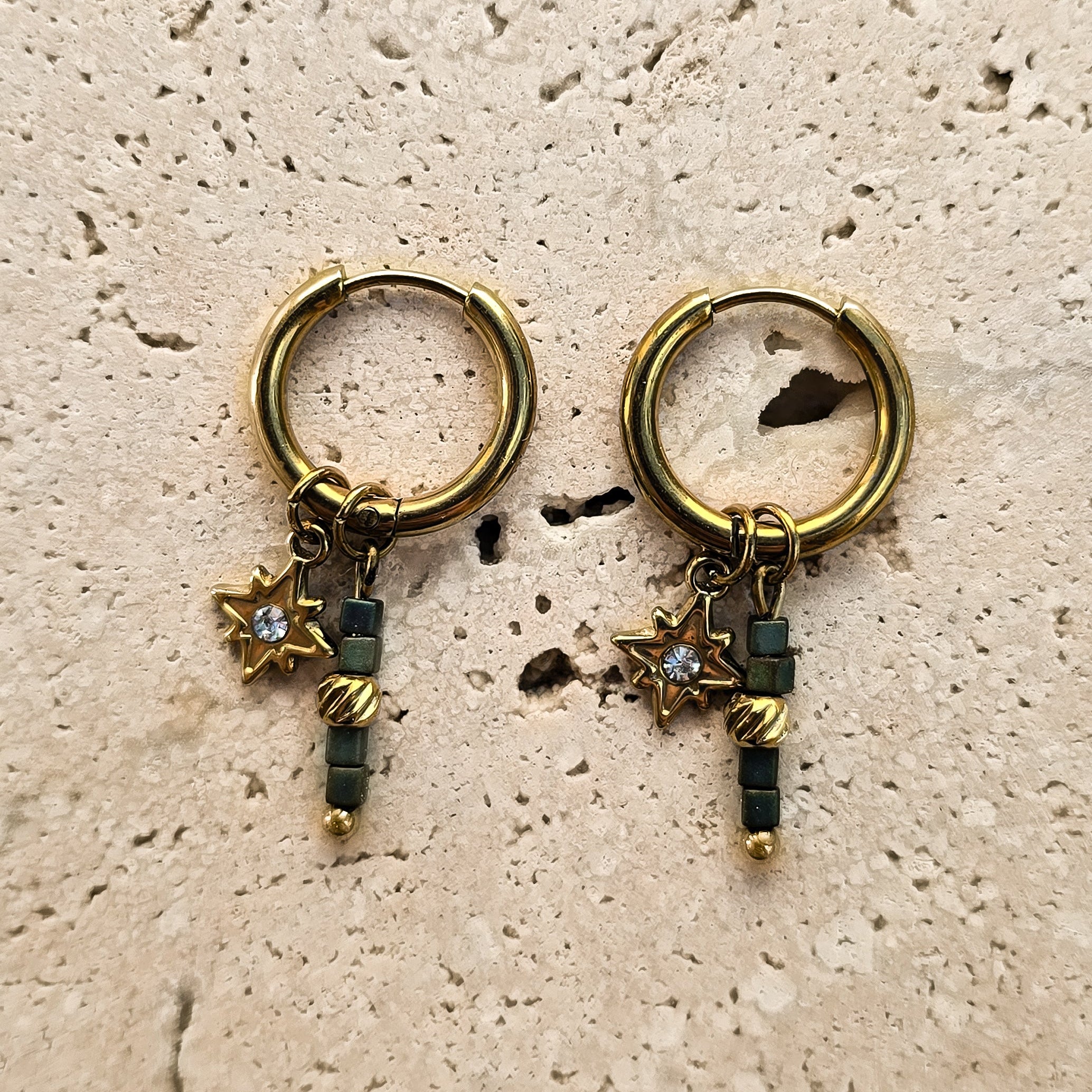 Boucles d’oreilles créoles dorées en acier inoxydable avec étoile et perles en verre bleu-vert sur fond minéral