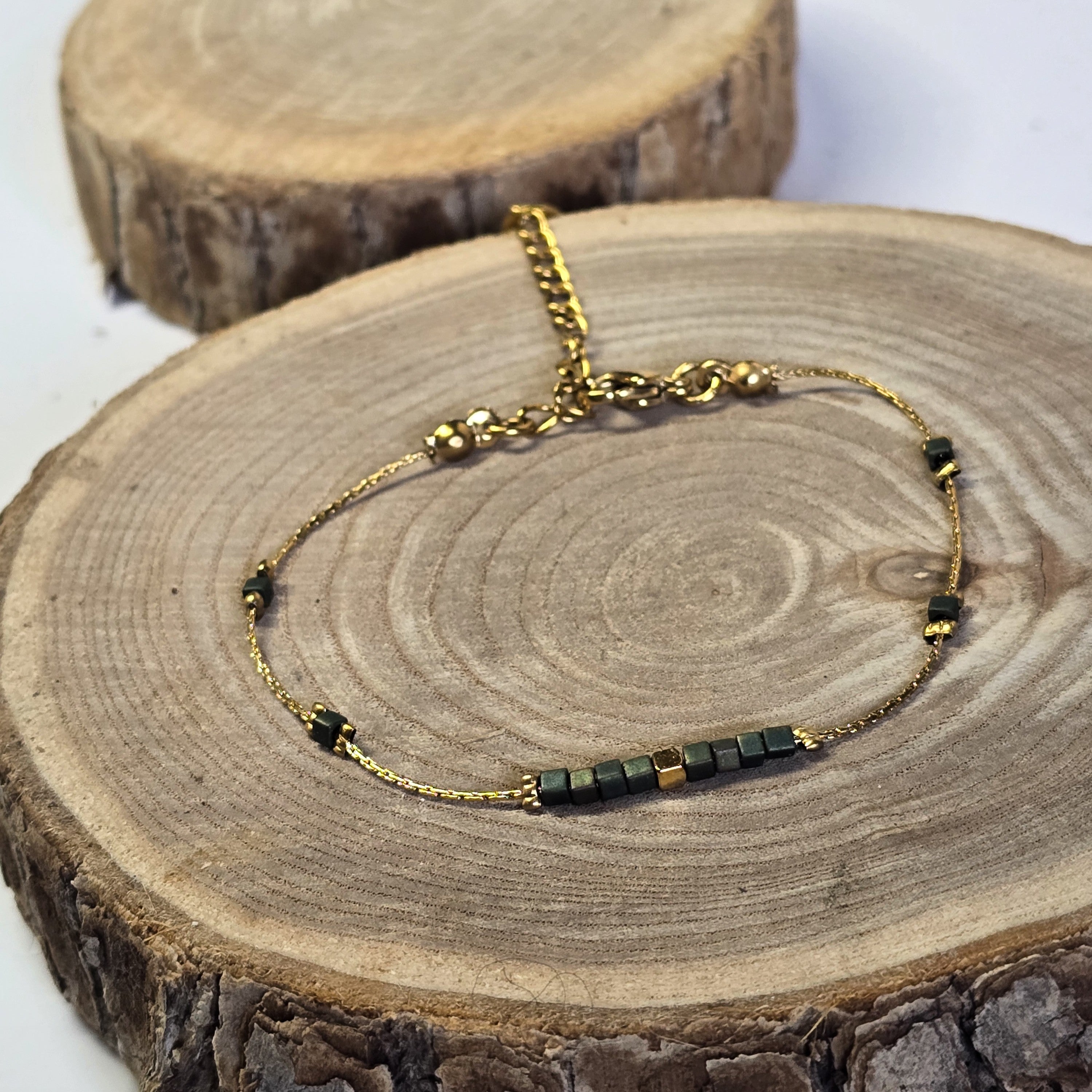 Bracelet fin en acier inoxydable doré avec perles en verre irisées vert bleu sur support bois - Clyvia Bijoux