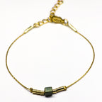 Bracelet doré en acier inoxydable orné d’une perle en verre irisée bleu-vert, bijou minimaliste et élégant signé Clyvia Bijoux.