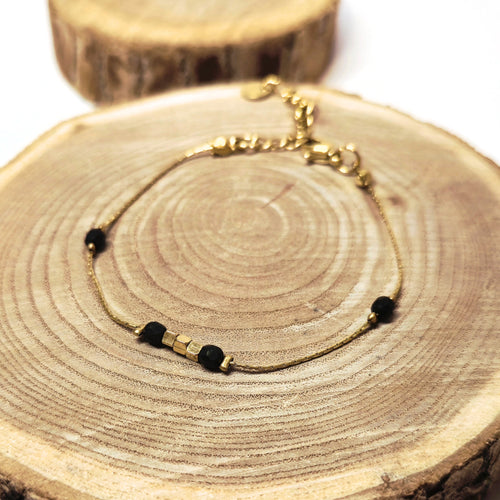 Bracelet doré en acier inoxydable avec perles noires facettées et perles dorées posé sur fond bois, bijou raffiné et moderne Clyvia Bijoux.