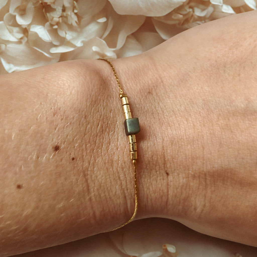 Bracelet fin doré en acier inoxydable avec une perle en verre irisée aux reflets bleu-vert, bijou délicat porté au poignet, création Clyvia Bijoux.