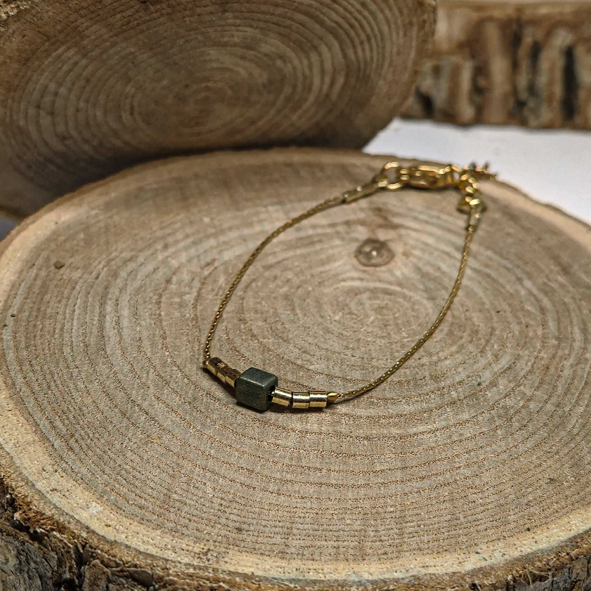 Bracelet fin doré avec perle irisée aux reflets bleu-vert posé sur bois, bijou raffiné et lumineux Clyvia Bijoux.