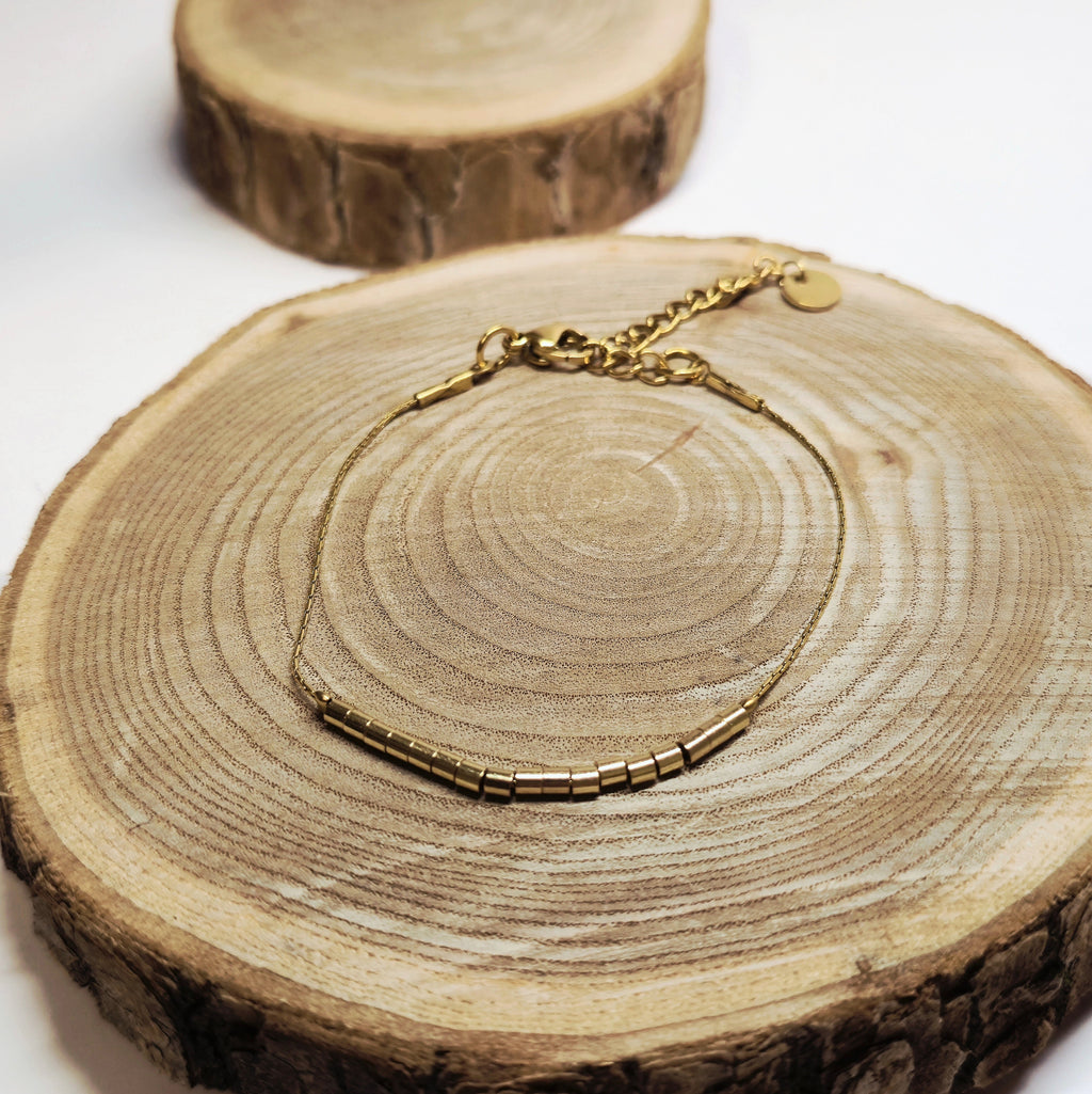 Bracelet doré minimaliste avec perles tubes dorées posé sur bois, bijou raffiné et intemporel Clyvia Bijoux.