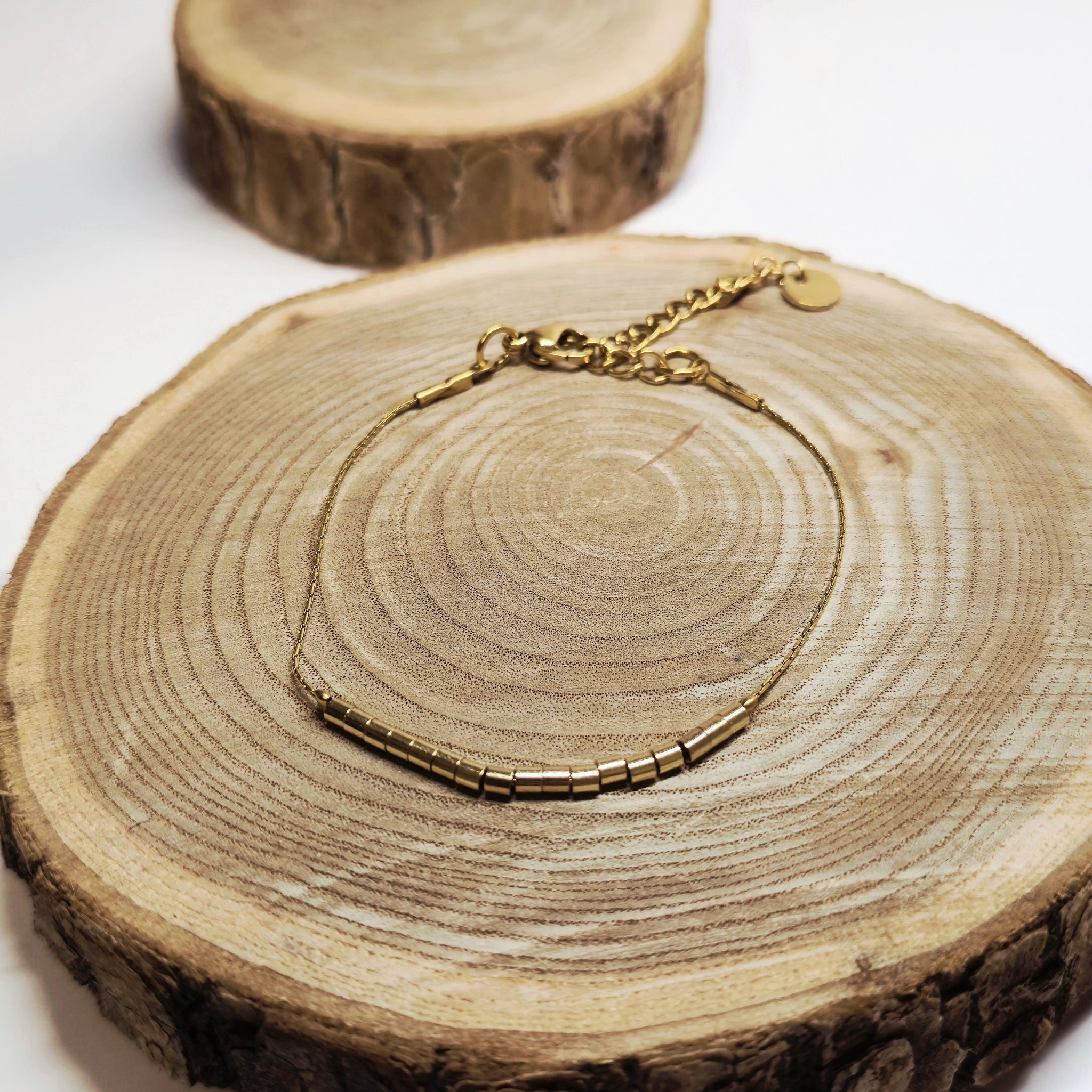 Bracelet doré minimaliste avec perles tubes dorées posé sur bois, bijou raffiné et intemporel Clyvia Bijoux.