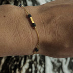 Bracelet fin doré en acier inoxydable orné de perles noires facettées et de perles dorées cubiques, bijou élégant porté au poignet, création Clyvia Bijoux.