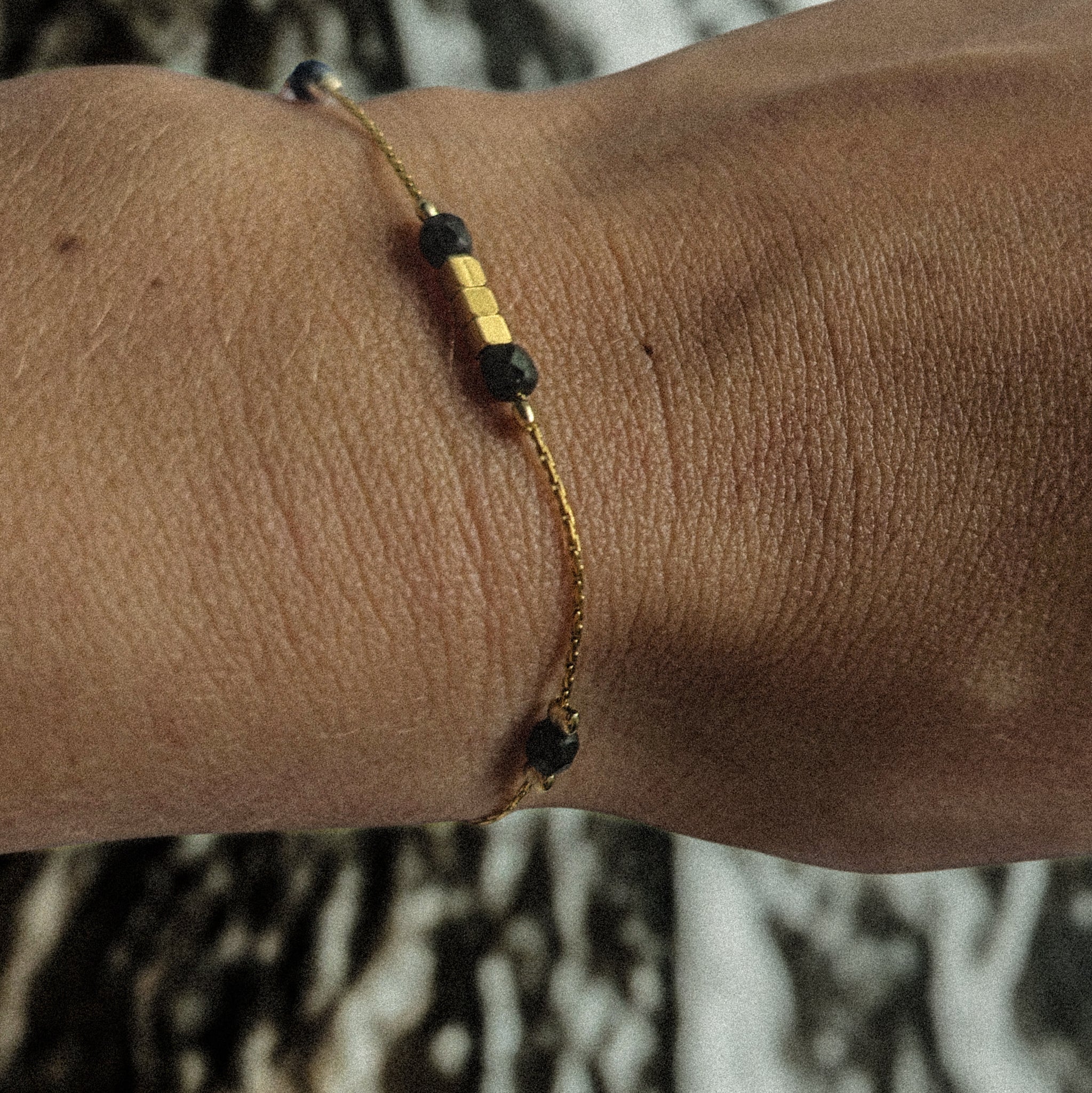 Bracelet fin doré en acier inoxydable orné de perles noires facettées et de perles dorées cubiques, bijou élégant porté au poignet, création Clyvia Bijoux.