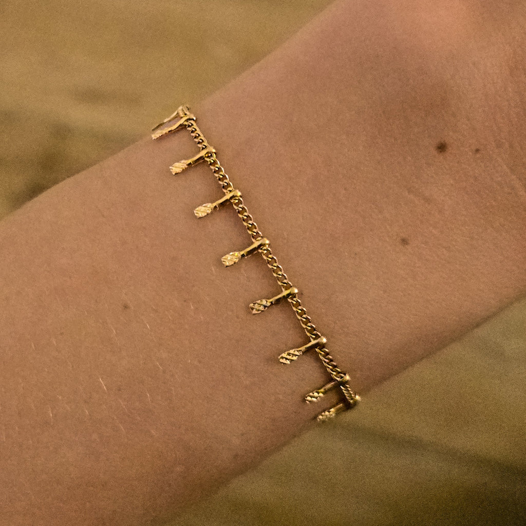 Bracelet doré fin à petites pampilles texturées, porté au poignet