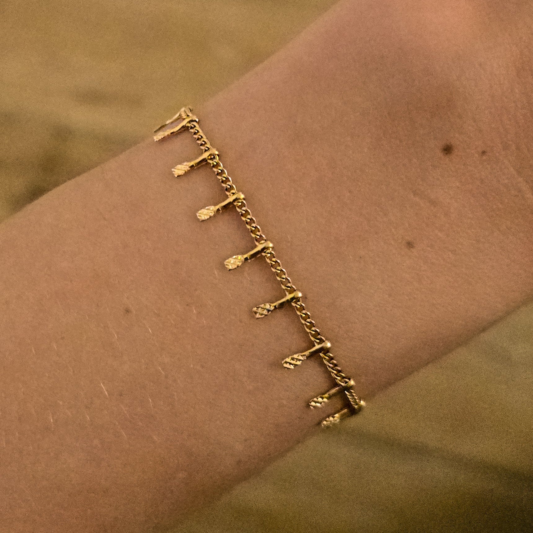 Bracelet doré fin à petites pampilles texturées, porté au poignet
