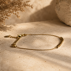 Bracelet doré fin avec perles carrées et fermoir réglable sur fond pierre