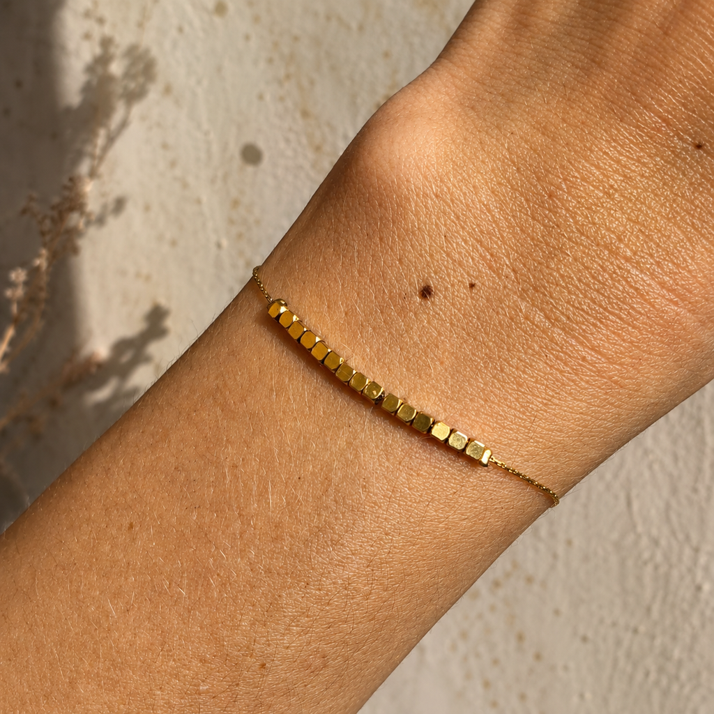 Bracelet doré porté au poignet avec rangée de perles carrées minimalistes