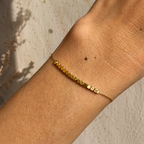 Bracelet doré porté au poignet avec rangée de perles carrées minimalistes