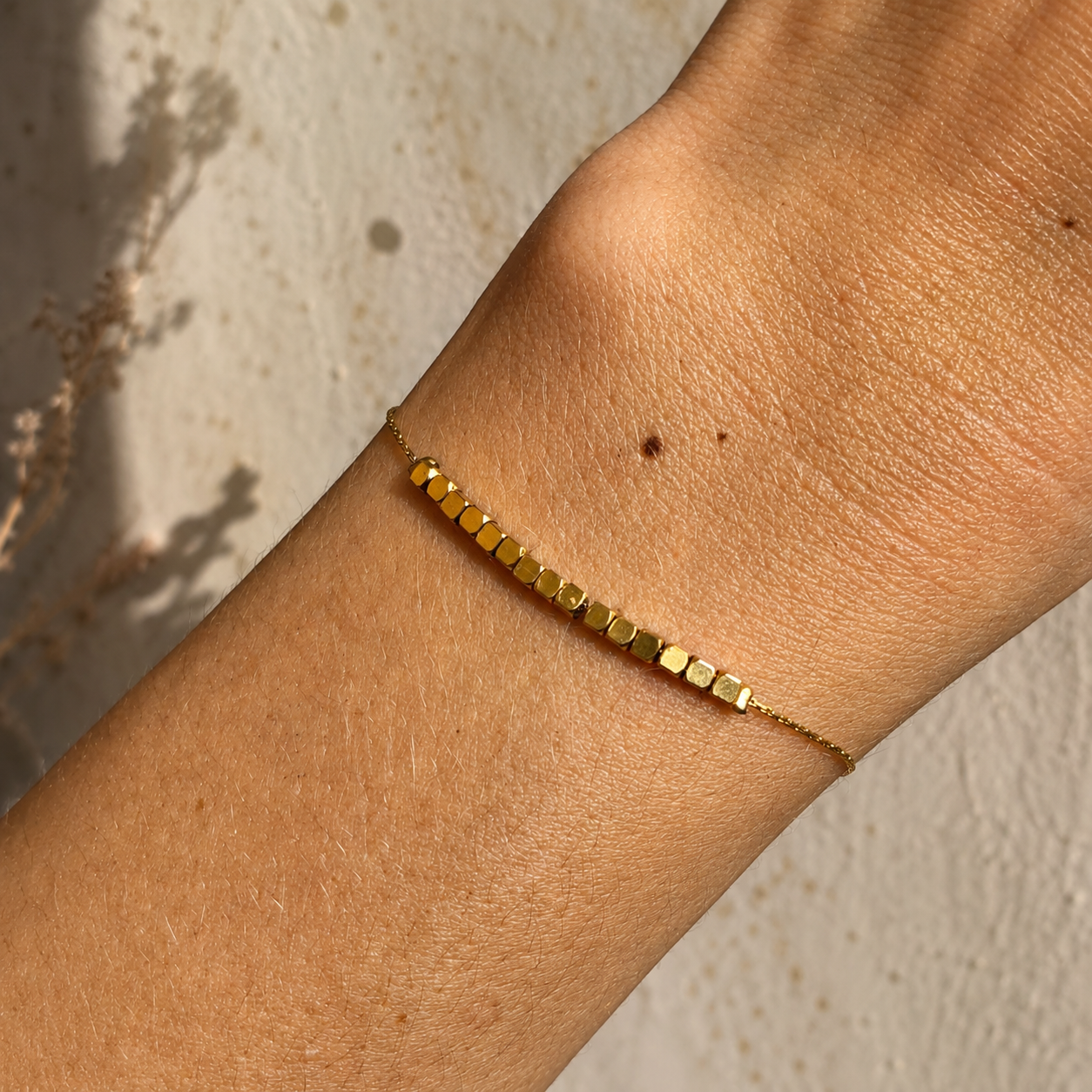 Bracelet doré porté au poignet avec rangée de perles carrées minimalistes