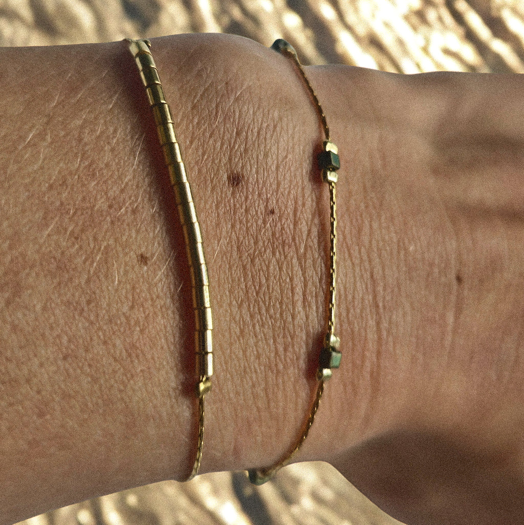 Bracelet fin doré avec perles irisées vert-bleu porté au poignet, bijou féminin élégant et discret Clyvia Bijoux.