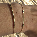 Bracelet fin doré avec perles irisées vert-bleu porté au poignet, bijou féminin élégant et discret Clyvia Bijoux.