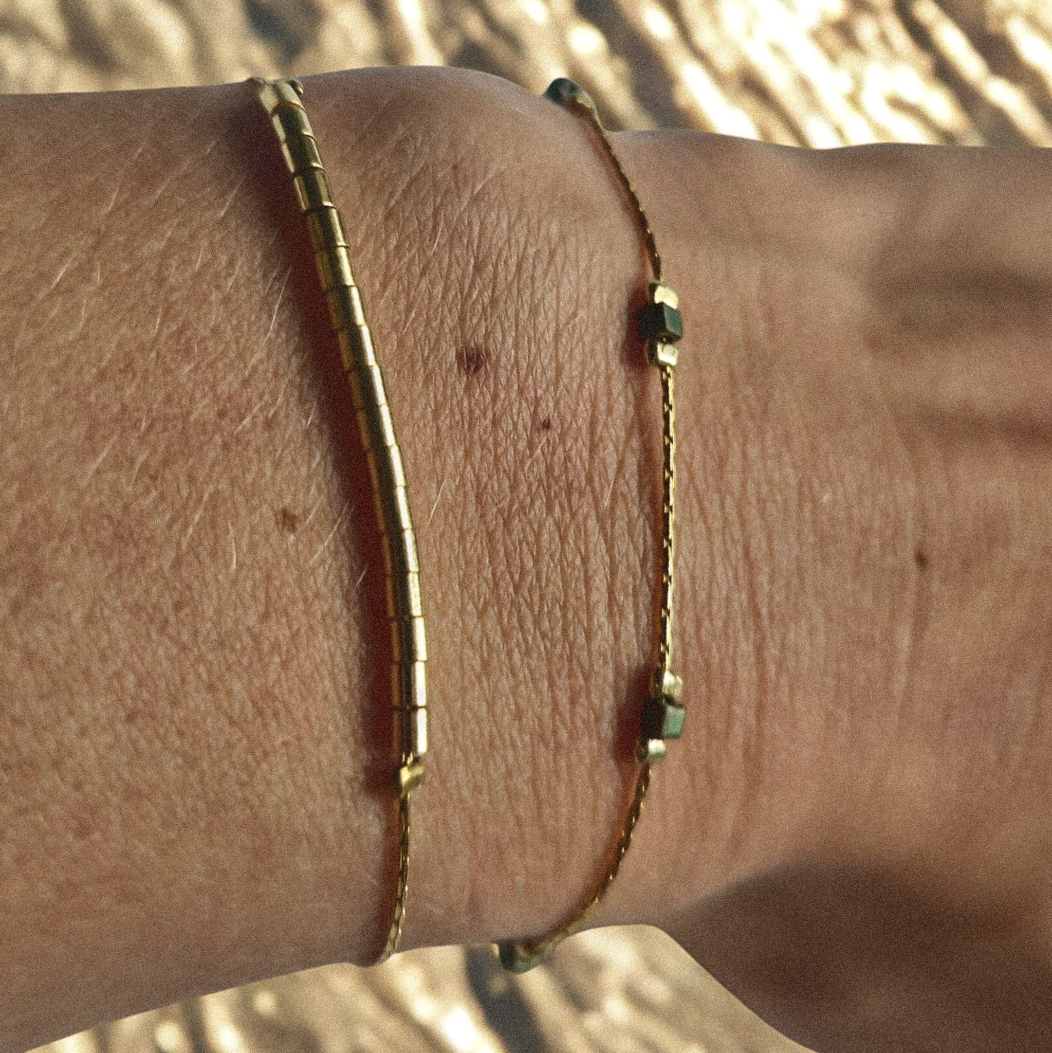 Bracelet fin doré avec perles irisées vert-bleu porté au poignet, bijou féminin élégant et discret Clyvia Bijoux.