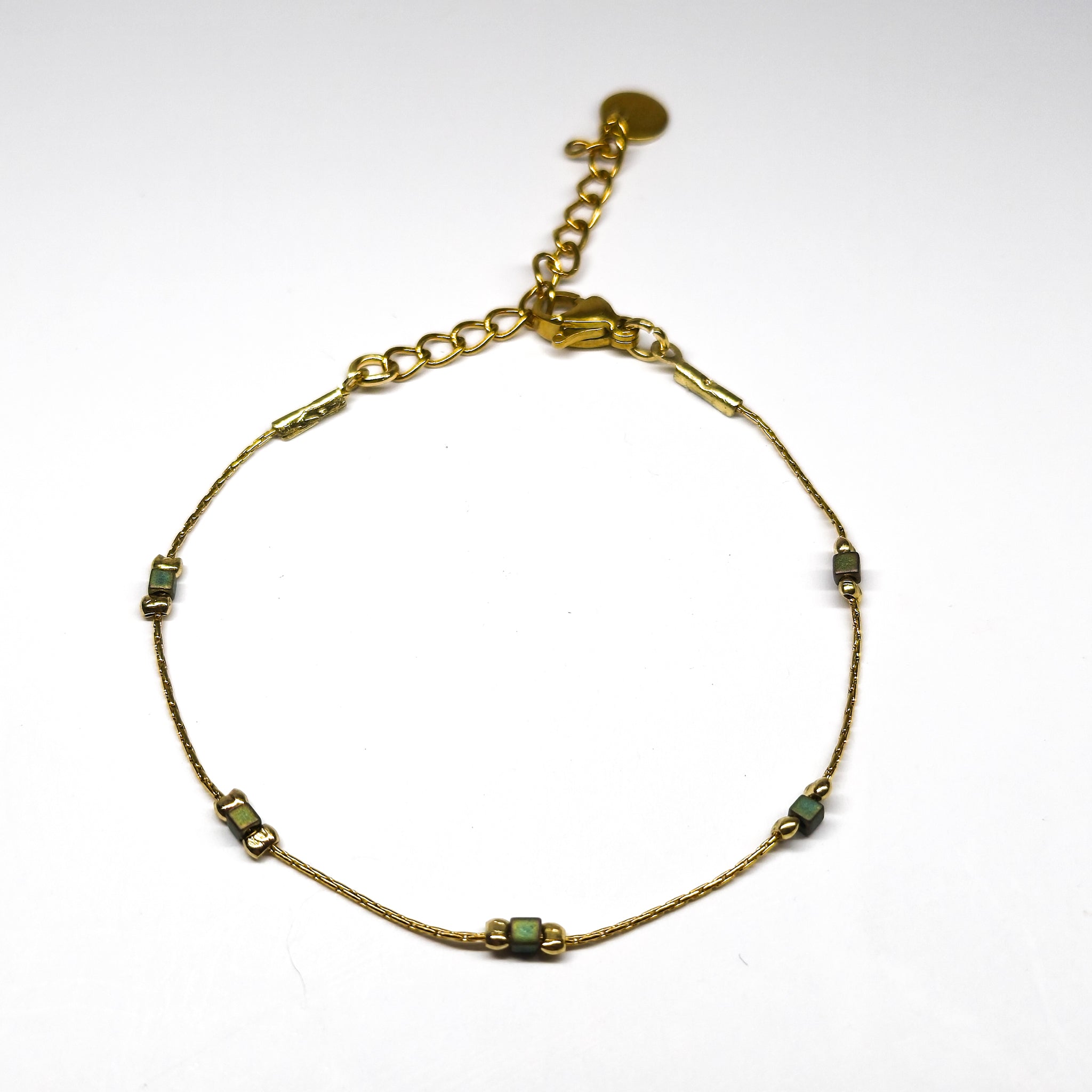 Bracelet fin doré en acier inoxydable avec petites perles irisées vert-bleu, bijou délicat et lumineux signé Clyvia Bijoux.