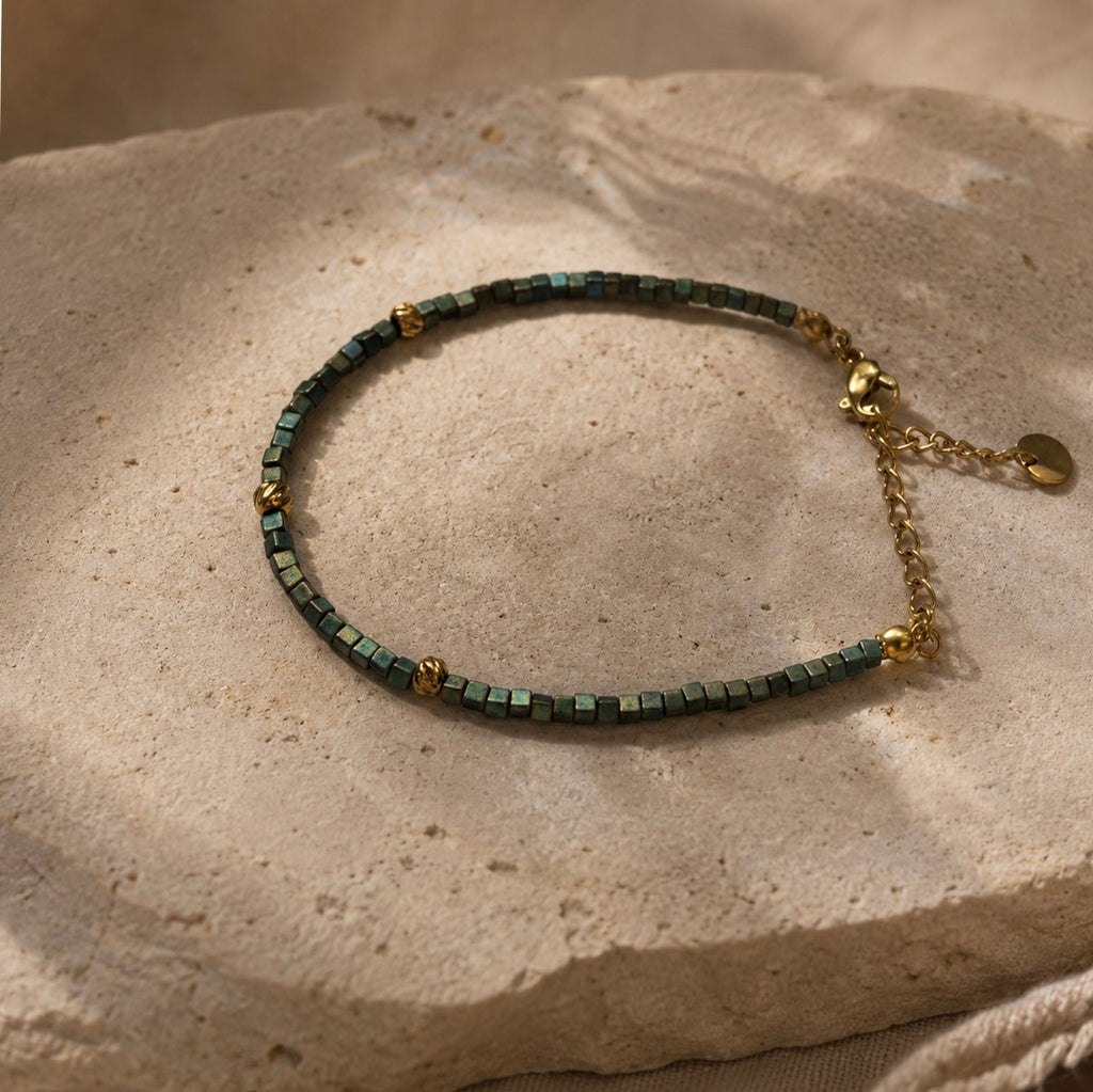 Bracelet ajustable en perles Miyuki bleu-vert irisées posé sur fond minéral