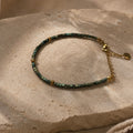 Bracelet ajustable en perles Miyuki bleu-vert irisées posé sur fond minéral