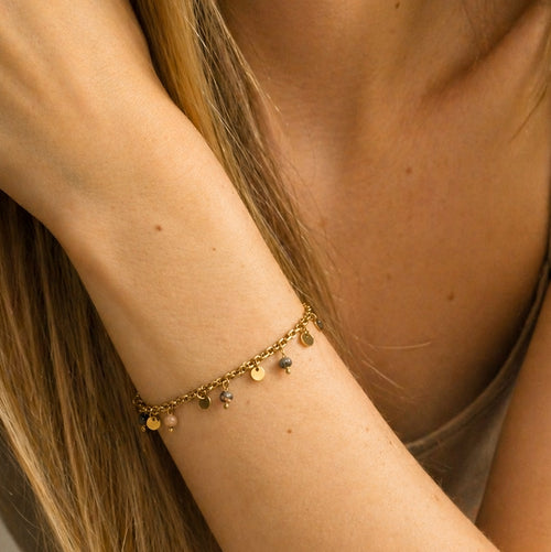 Bracelet en rhodonite naturelle porté au poignet avec chaîne dorée et pampilles