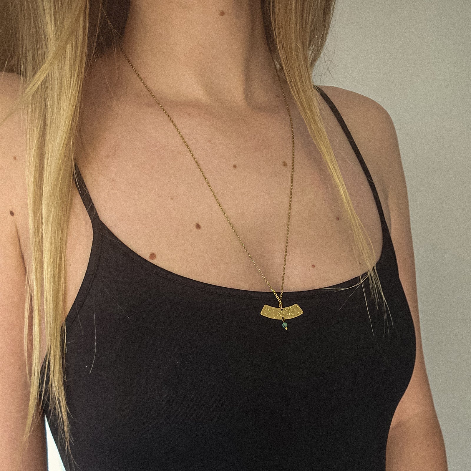 Collier long doré avec pendentif martelé et jaspe porté sur top noir