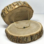 Collier doré en acier inoxydable pour femme, posé sur rondin bois pour ambiance nature, design épuré et lumineux — marque Clyvia Bijoux.