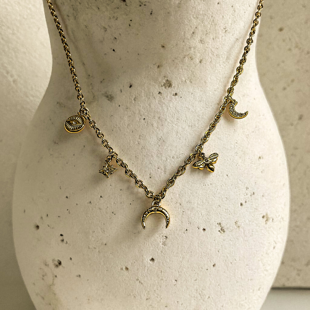 Collier doré à breloques sur présentoir minéral, inspiration bijoux Clyvia Bijoux