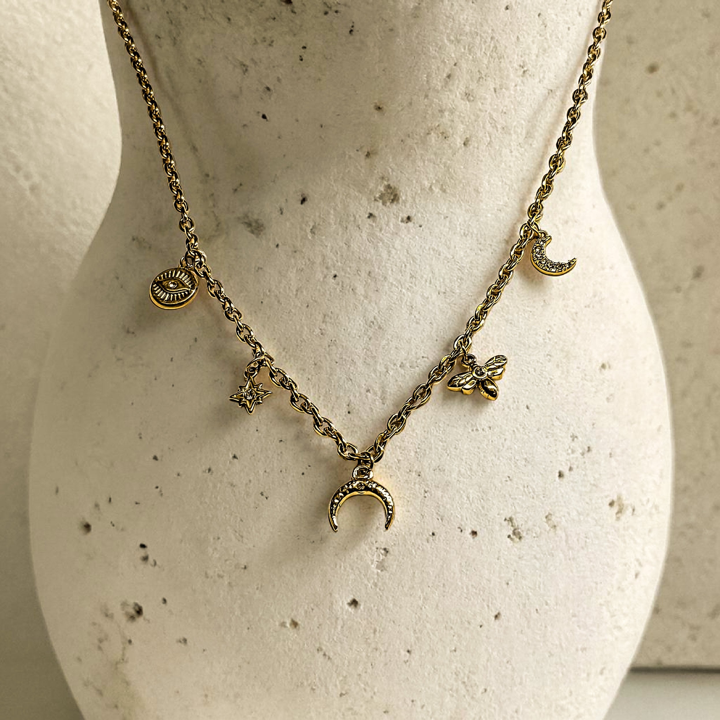 Collier doré à breloques en acier inoxydable sur présentoir avec lune, œil, étoile, libellule et demi-corne