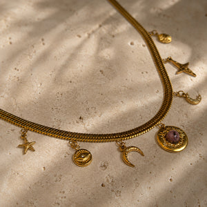 Détail d’un collier doré à breloques étoile, lune, oeil et pendentif soleil avec pierre rose