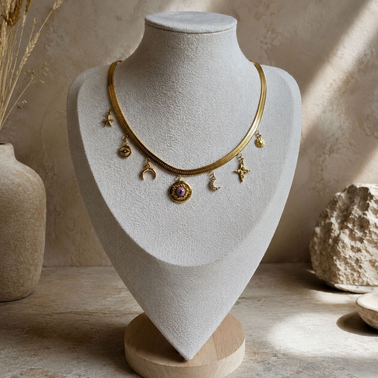 Collier doré à breloques célestes avec étoile, lune, oeil et pendentif soleil à pierre rose sur présentoir