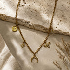Collier doré à breloques lune, oeil, étoile et fleur sur fond pierre