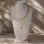 Collier doré à pendentif étoile présenté en superposition avec une chaîne plate sur un buste beige.