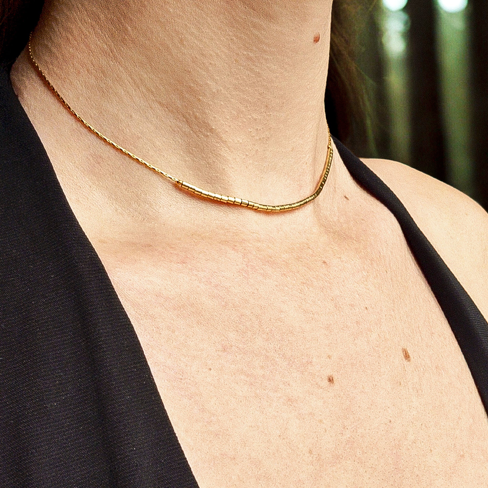 Collier ras de cou fin doré en acier inoxydable porté au cou, orné de petites perles cylindriques dorées, bijou minimaliste et élégant signé Clyvia Bijoux.