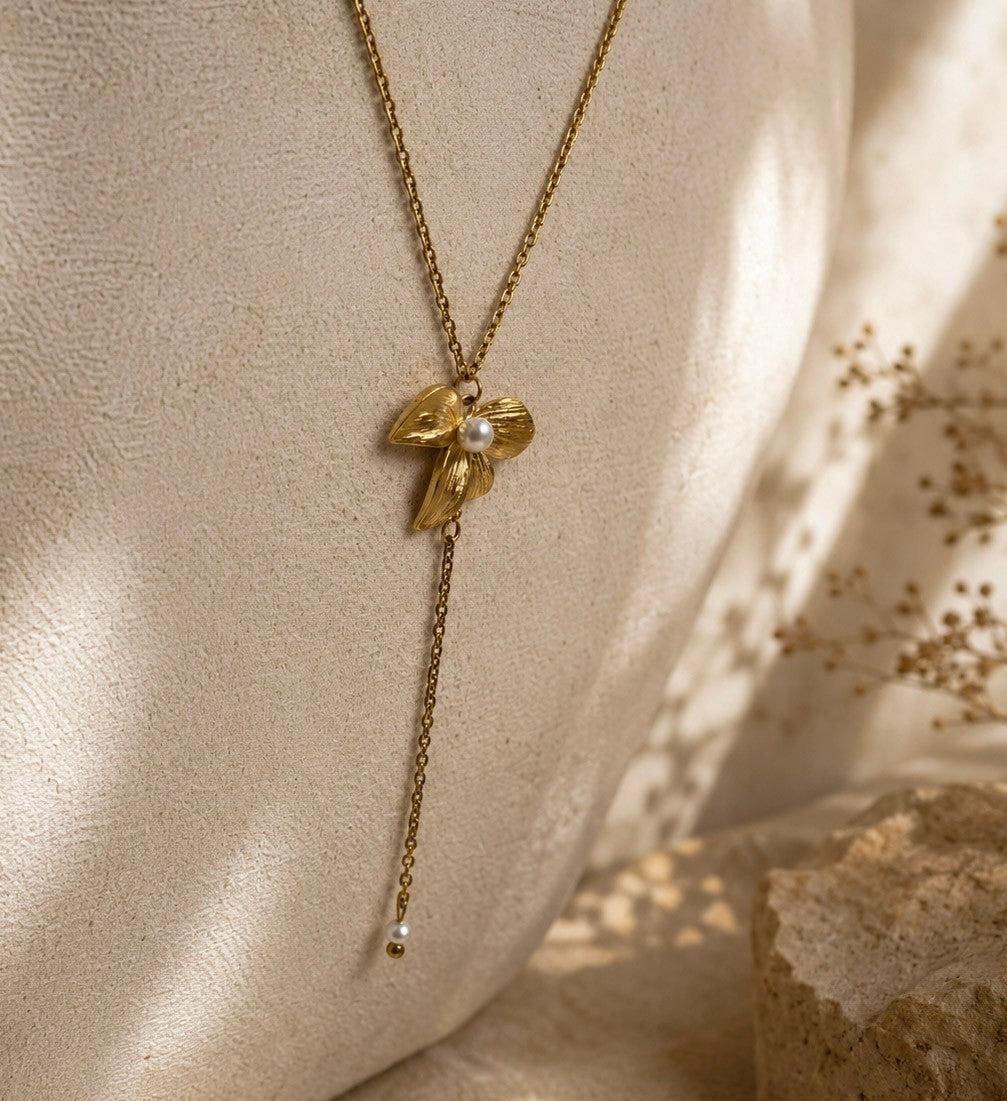 Collier doré pendentif fleur avec perle blanche suspendu devant un mur texturé