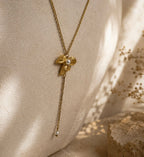 Collier doré pendentif fleur avec perle blanche suspendu devant un mur texturé