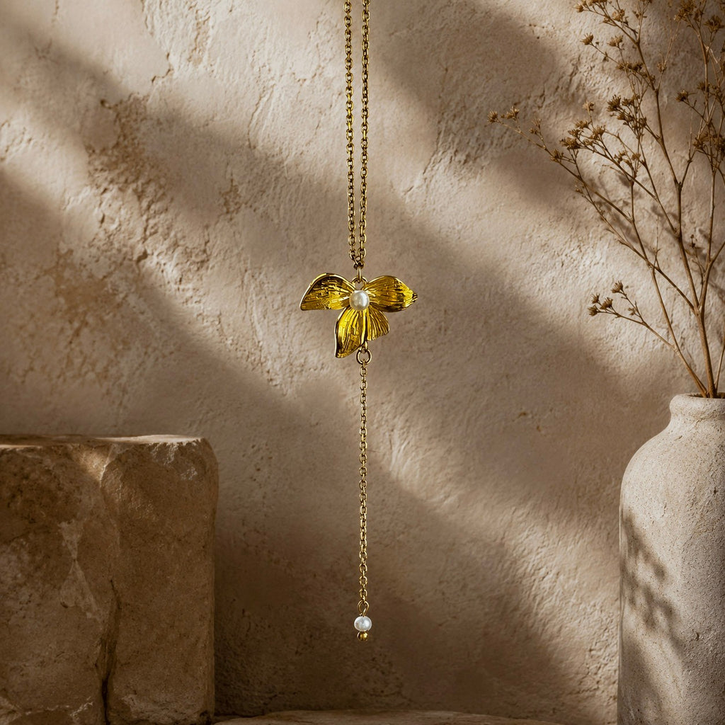Détail d’un collier doré avec pendentif fleur texturé, perle blanche et chaîne pendante
