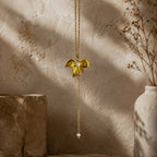 Détail d’un collier doré avec pendentif fleur texturé, perle blanche et chaîne pendante