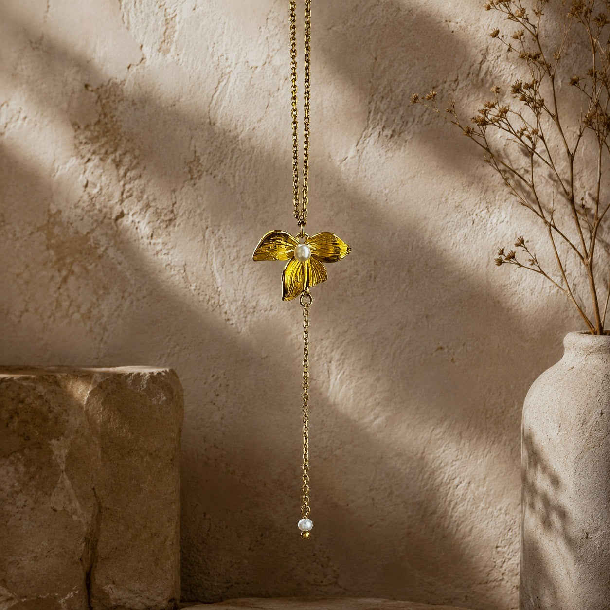 Détail d’un collier doré avec pendentif fleur texturé, perle blanche et chaîne pendante