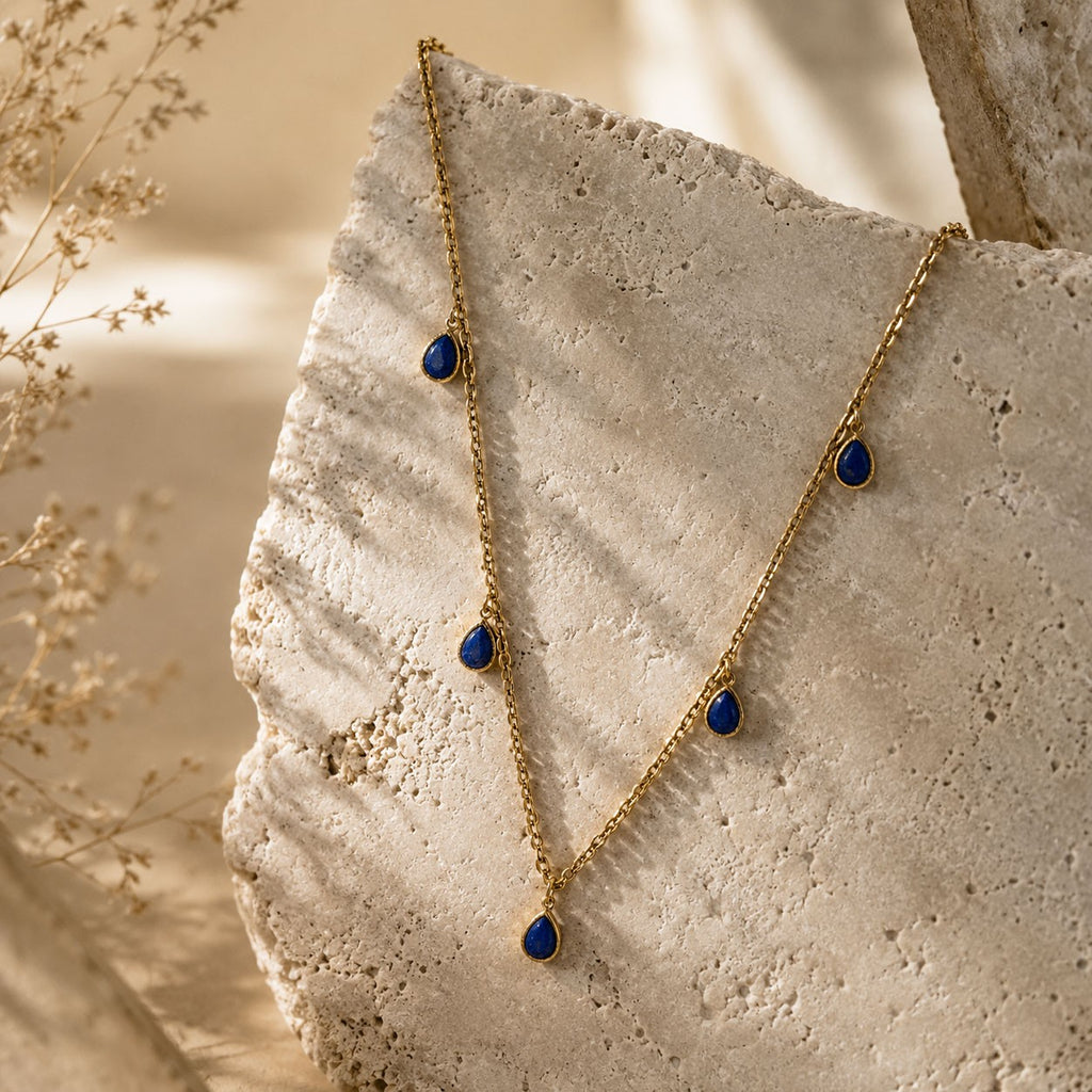 Collier doré avec pendentifs gouttes bleu lapis lazuli sur fond pierre