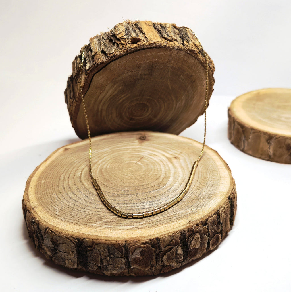 Collier ras-de-cou doré minimaliste en acier inoxydable décoré de perles tubes dorées posé sur fond bois, bijou raffiné et intemporel Clyvia Bijoux.