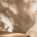 Collier doré avec pendentif croissant de lune photographié dans un décor beige lumineux.