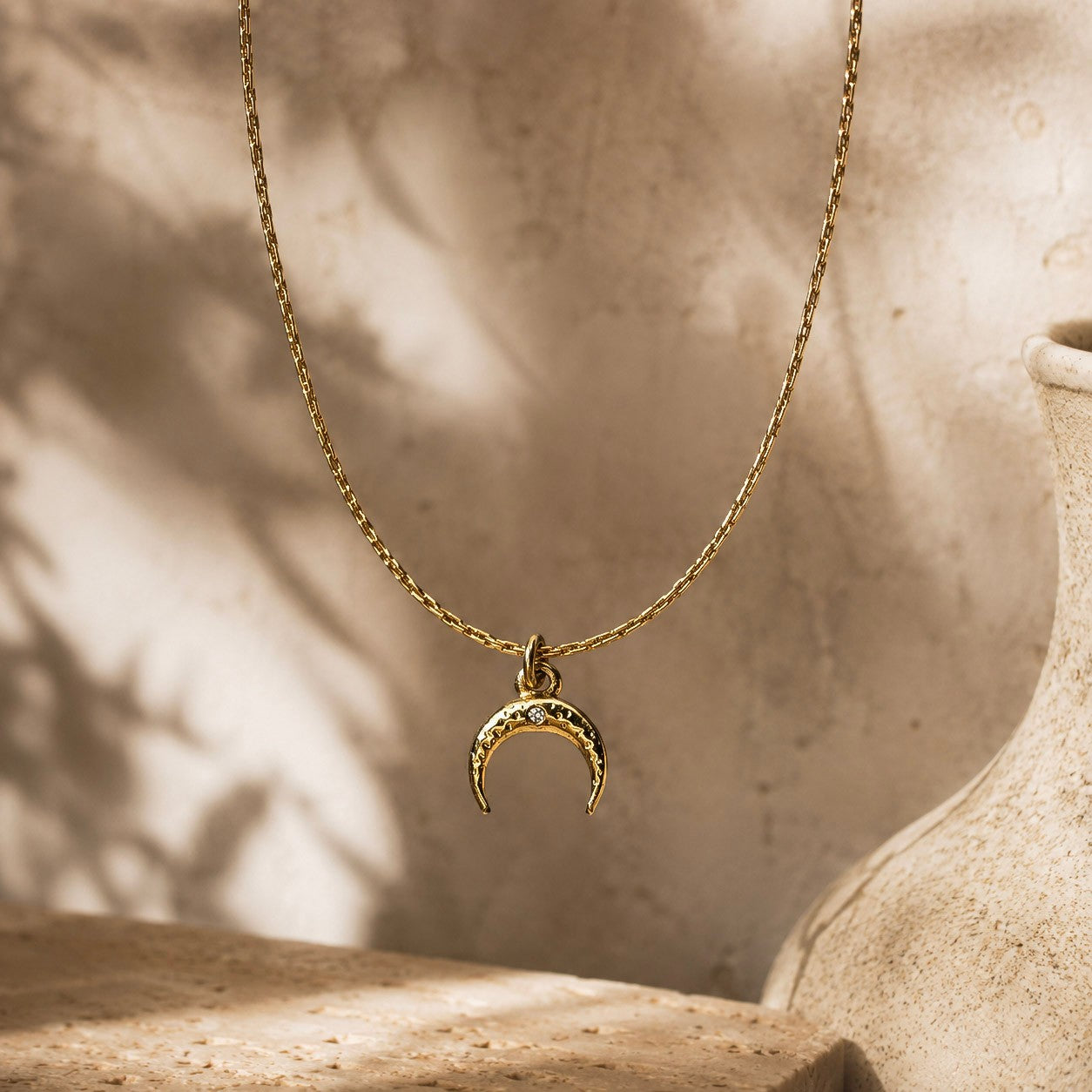 Collier doré avec pendentif croissant de lune photographié dans un décor beige lumineux.