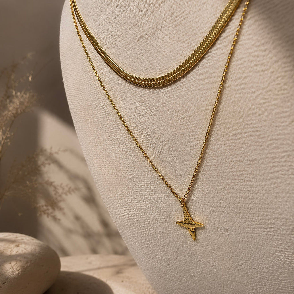 Collier doré à pendentif étoile présenté sur un buste avec une chaîne plate assortie.