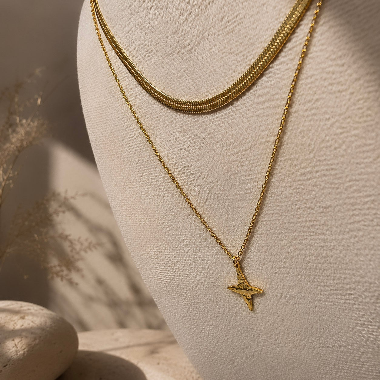 Collier doré à pendentif étoile présenté sur un buste avec une chaîne plate assortie.