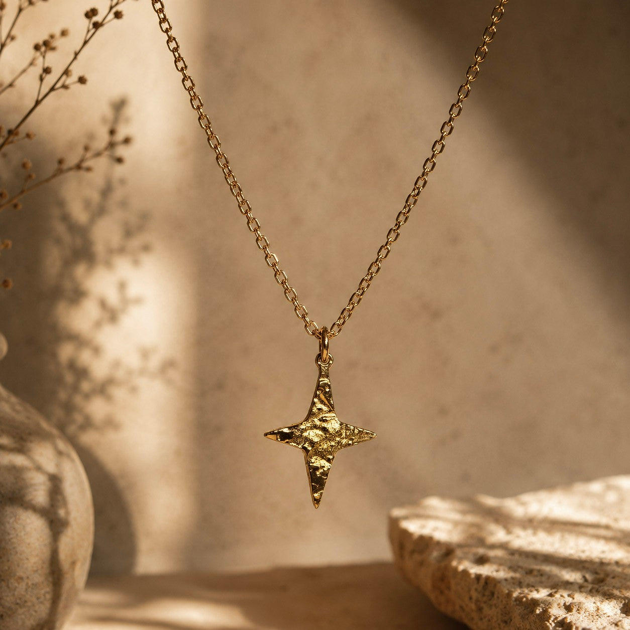 Gros plan sur un collier doré avec pendentif étoile martelé dans un décor aux tons beiges.