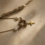 Détail d’un collier doré avec fermoir rond, pendentif étoile et perles blanches
