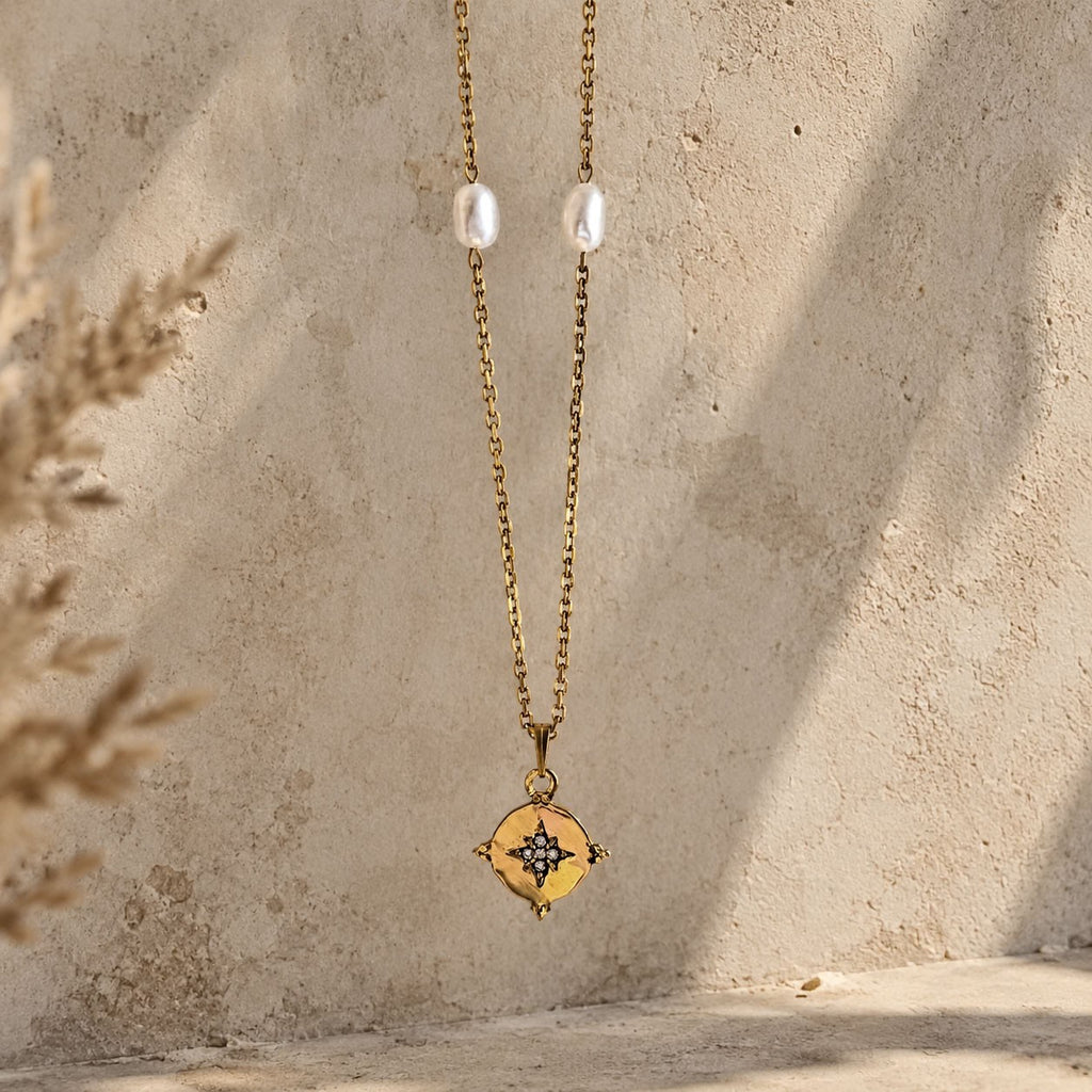 Collier doré avec pendentif étoile serti et perles blanches suspendu devant un mur texturé