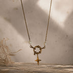 Collier doré avec pendentif étoile et perles blanches suspendu devant un fond texturé