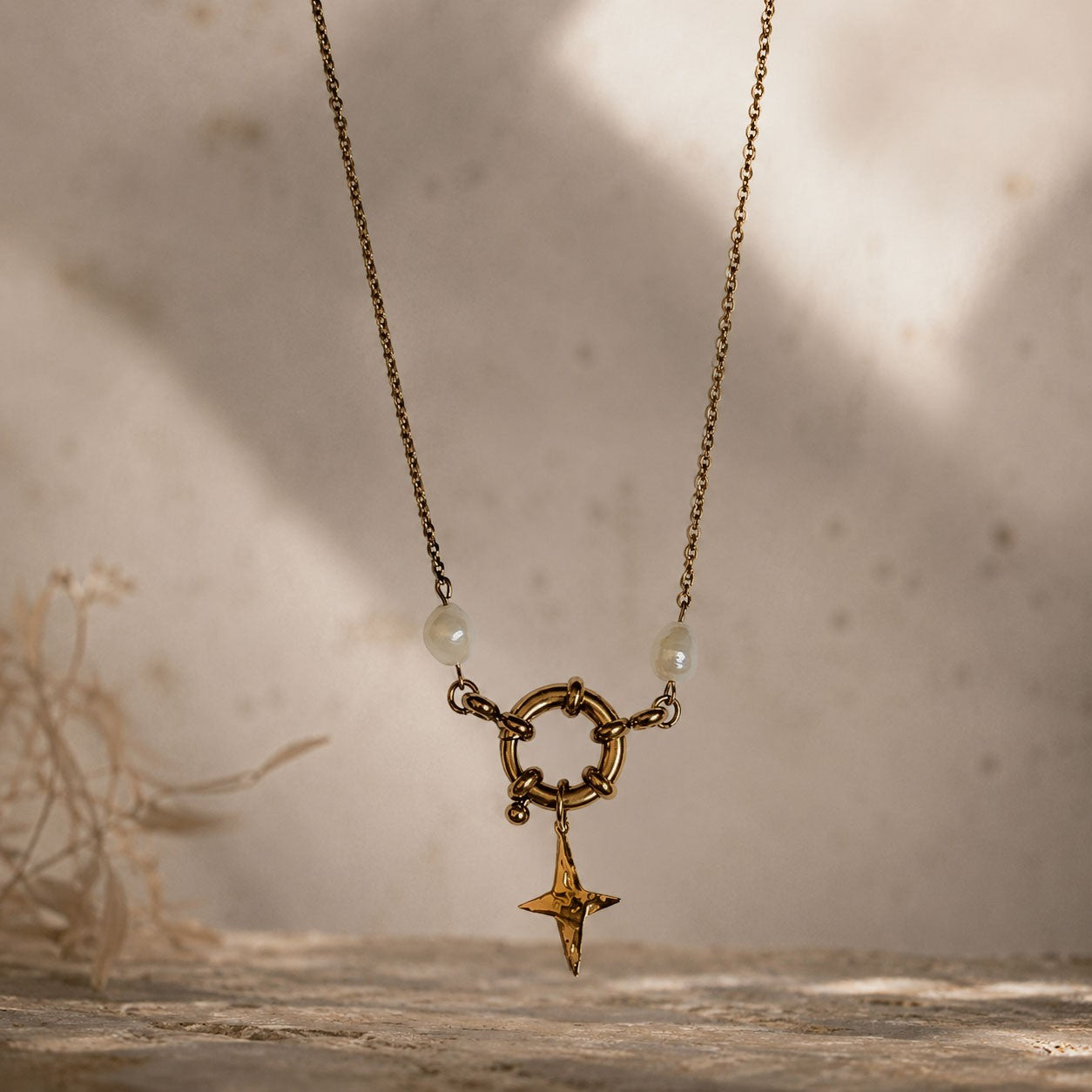 Collier doré avec pendentif étoile et perles blanches suspendu devant un fond texturé