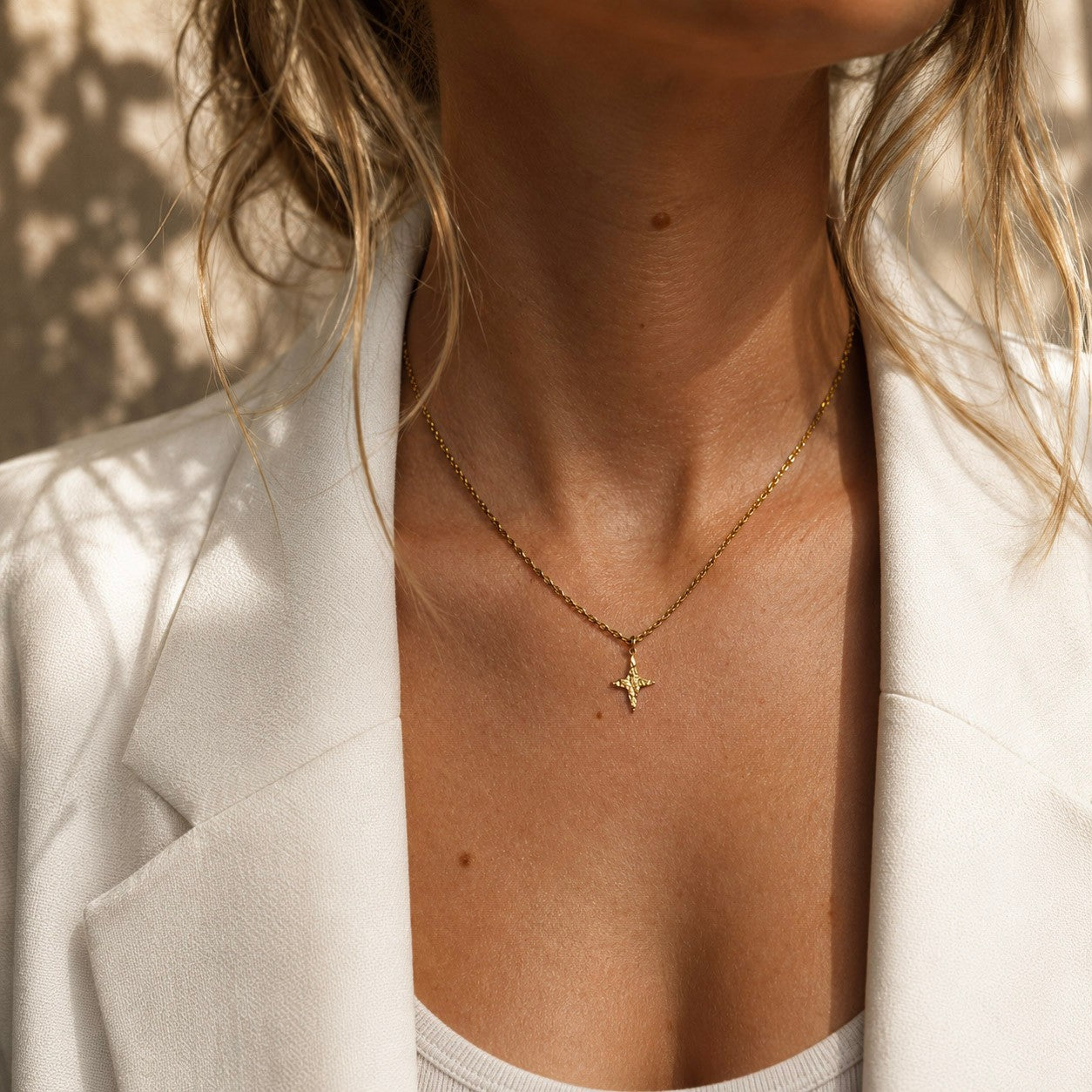 Femme portant un collier doré à pendentif étoile avec une veste blanche.