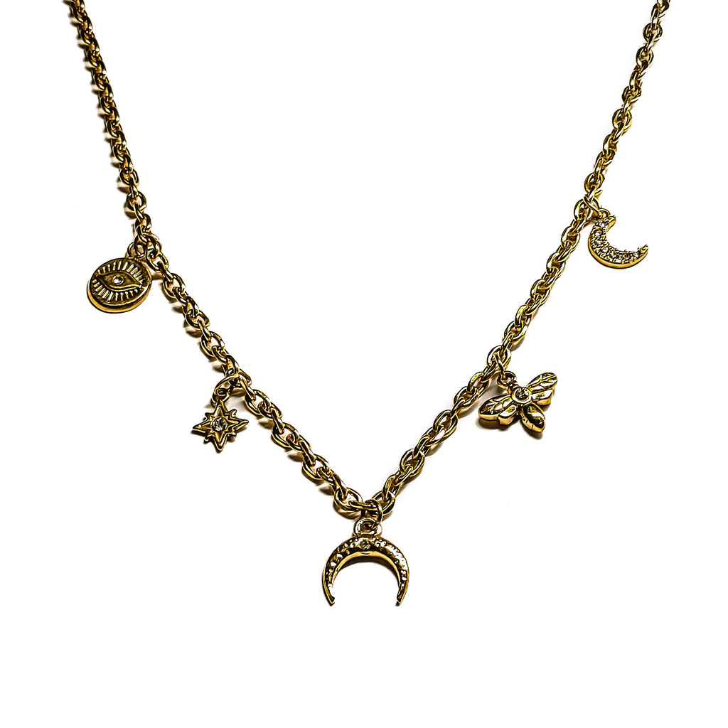 Détail d’un collier fin doré à breloques avec lune, œil, étoile, libellule et demi-corne